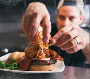 Bacon Cheese Burger in the kitchen window topped with frizzled onions by the chef.