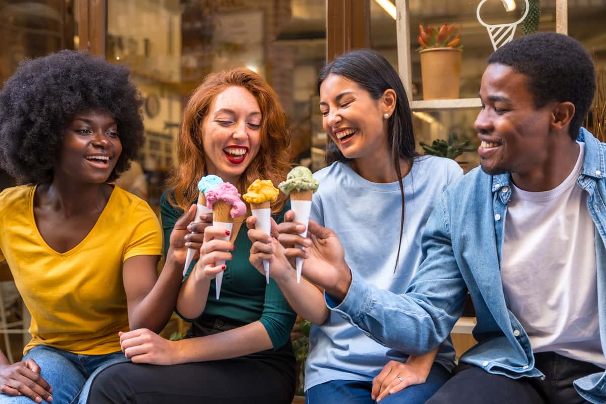Four friends enjoy ice cream cones together, laughing and smiling.