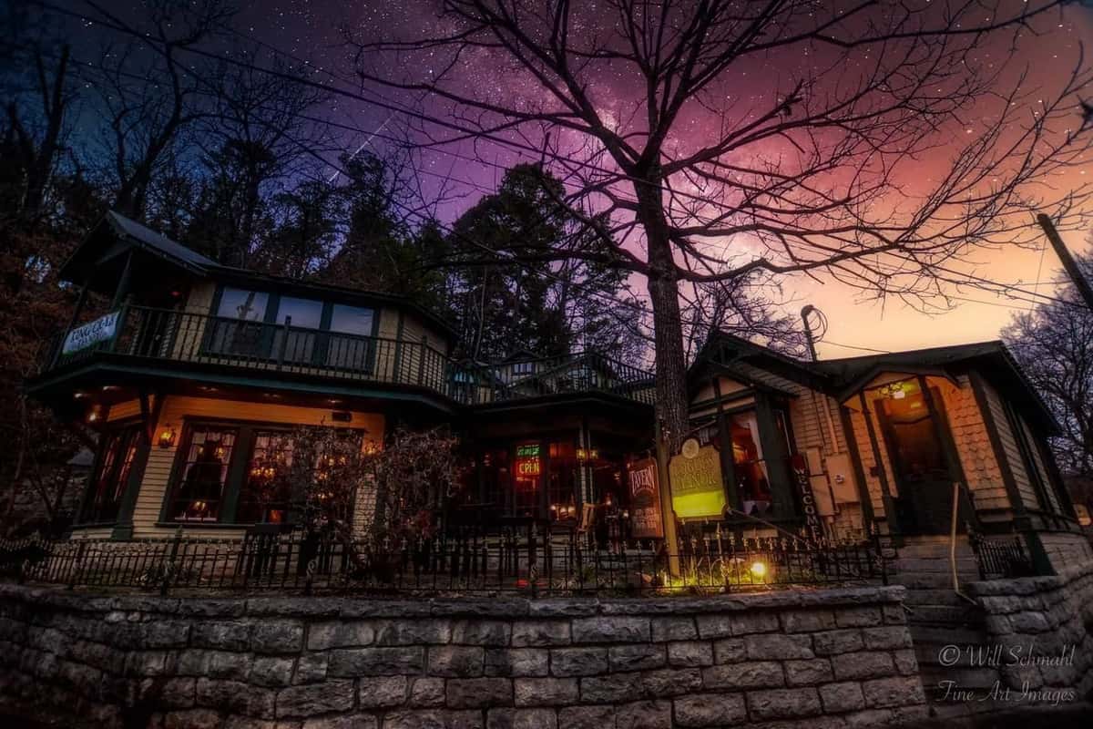 Charming, warmly lit restaurant with vintage architecture, nestled among trees under a vivid, starry twilight sky.