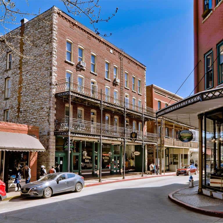 Historic downtown street lined with red-brick buildings featuring ornate wrought-iron balconies, local shops, and pedestrians.