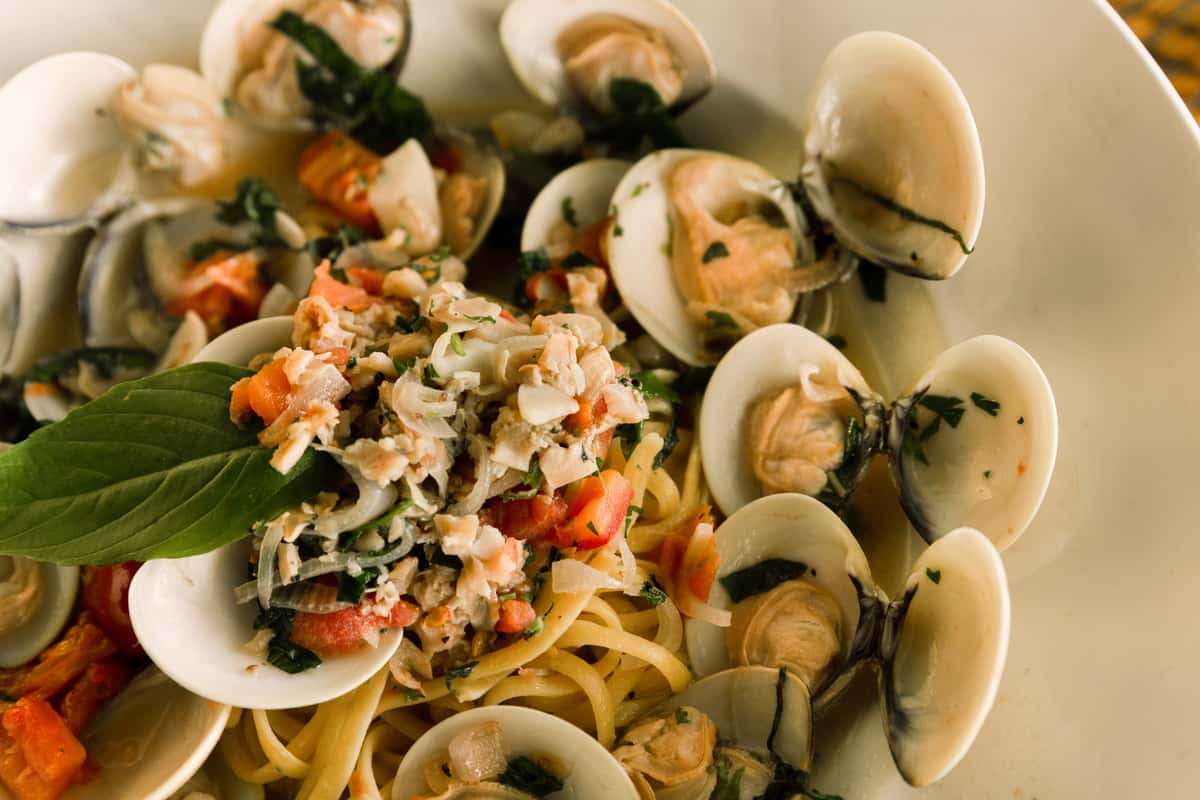 Close-up of seafood linguine with fresh clams in white wine sauce, topped with chopped herbs and diced tomatoes, served as a classic Italian seafood pasta dish.