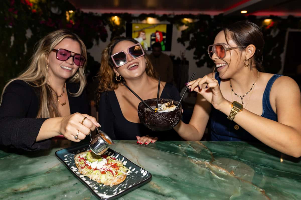 Three young women savoring a shareable cocktail and appetizer at the jade granite bar