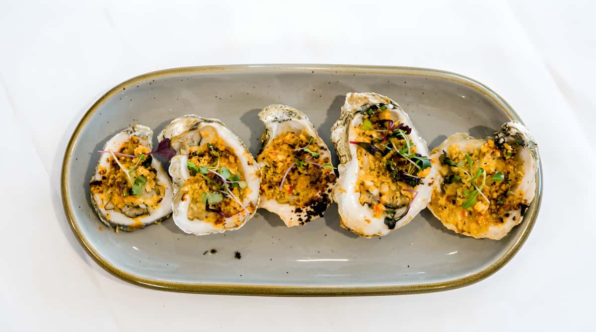 Baked oysters topped with herbs and breadcrumbs on an oval plate.