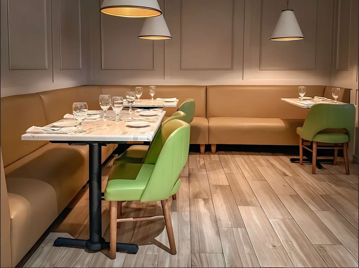 Modern restaurant dining room with booth seating, green chairs, and set tables.