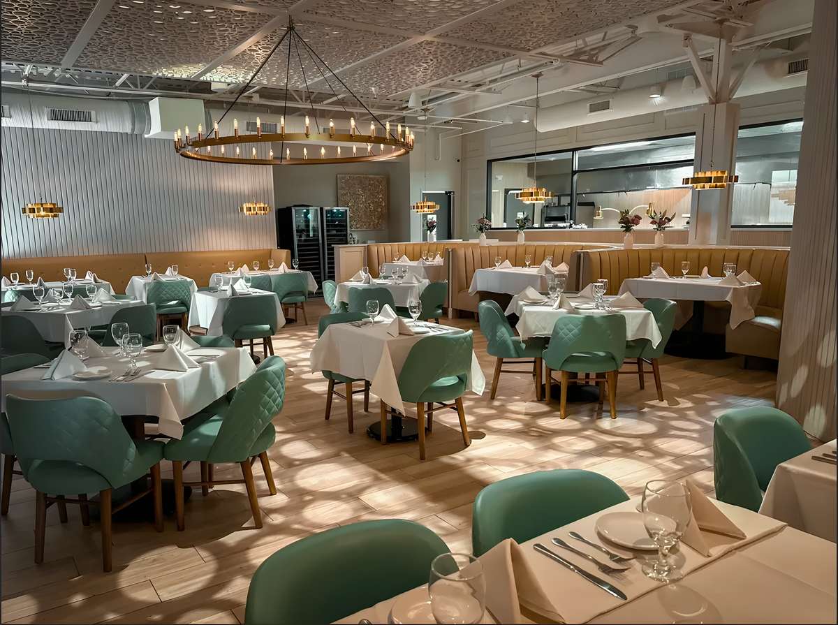 Elegant restaurant interior with white tablecloths, green chairs, and warm lighting.