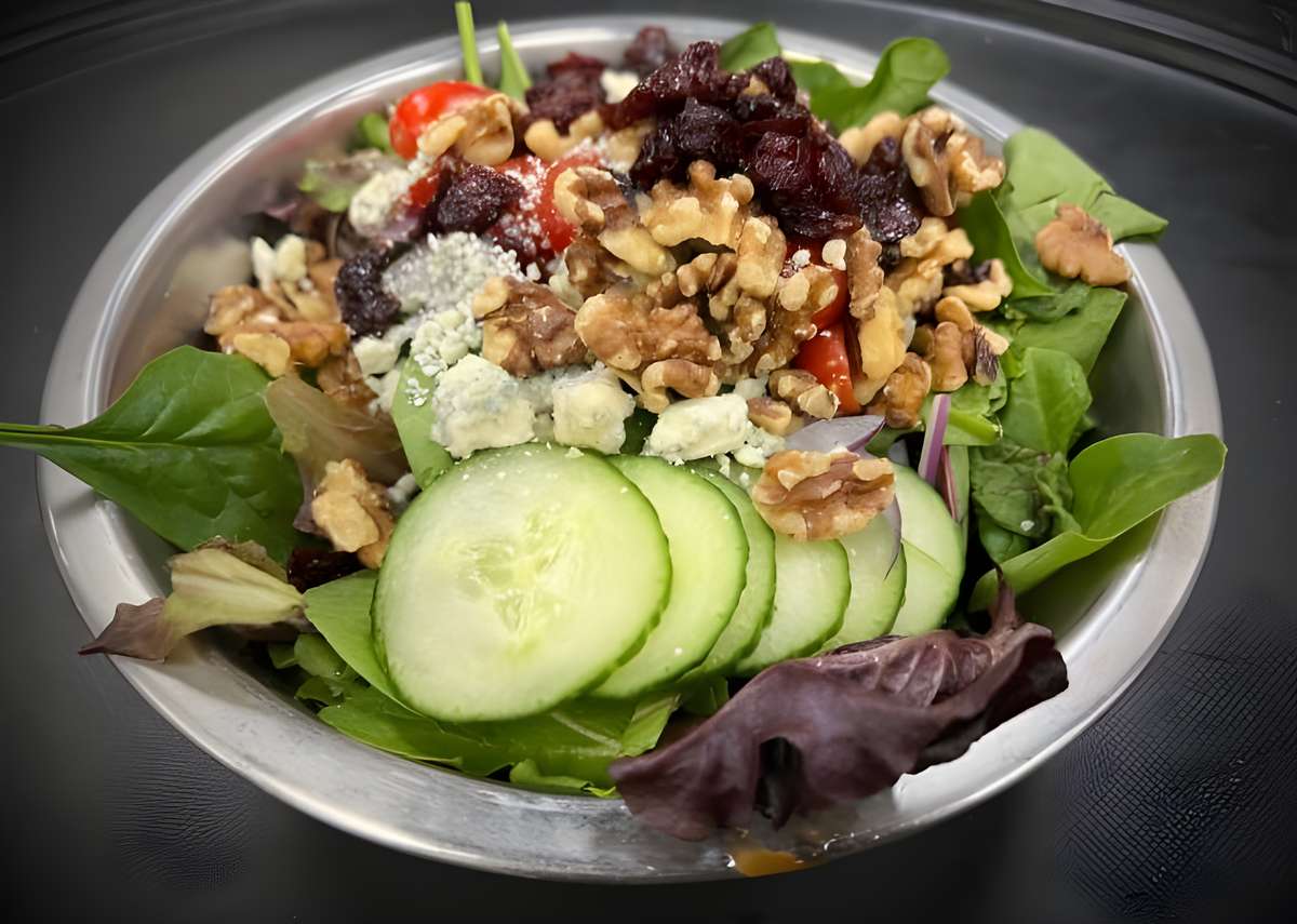 A gourmet salad featuring dark leafy greens, cucumber slices, walnuts, and crumbled blue cheese.