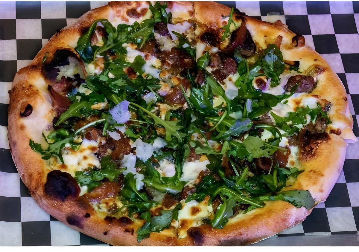 A thin-crust pizza topped with fresh green herbs, possibly pesto, and white cheese.