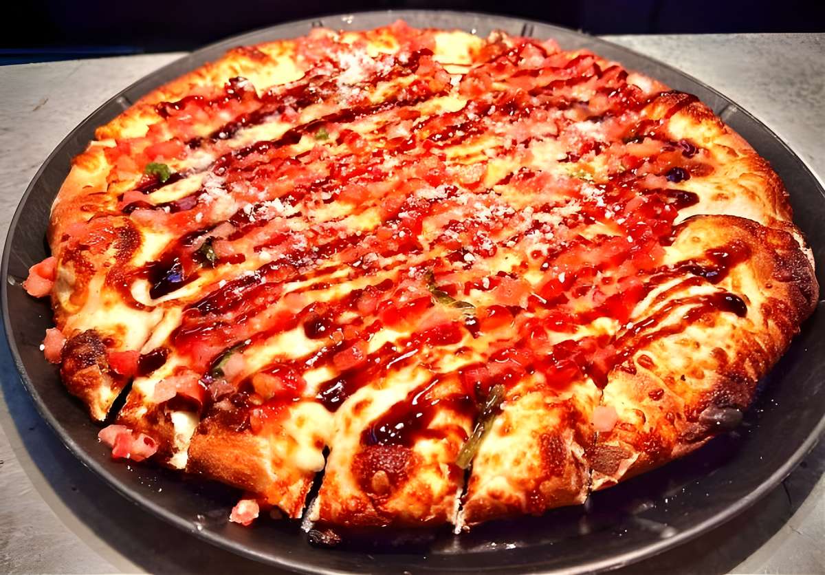 A pizza featuring a dark drizzle (likely BBQ sauce or balsamic glaze) over cheese and meat toppings.