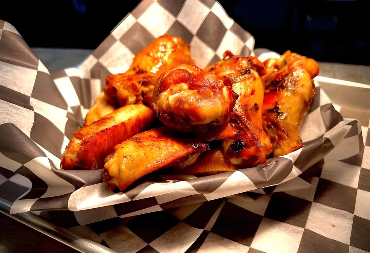 A basket of bone-in chicken wings tossed in a reddish glaze (likely buffalo or BBQ sauce).