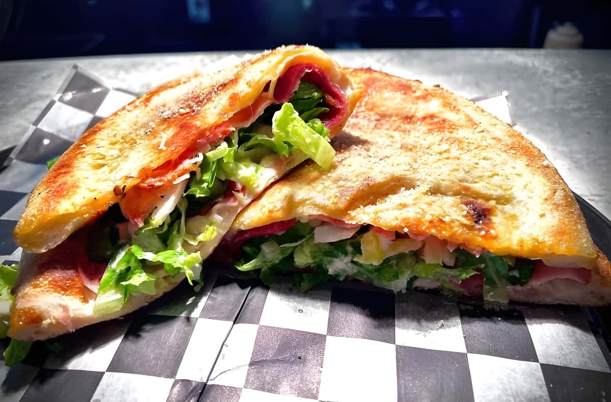 A toasted flatbread or pita sandwich filled with fresh greens and sliced meats.