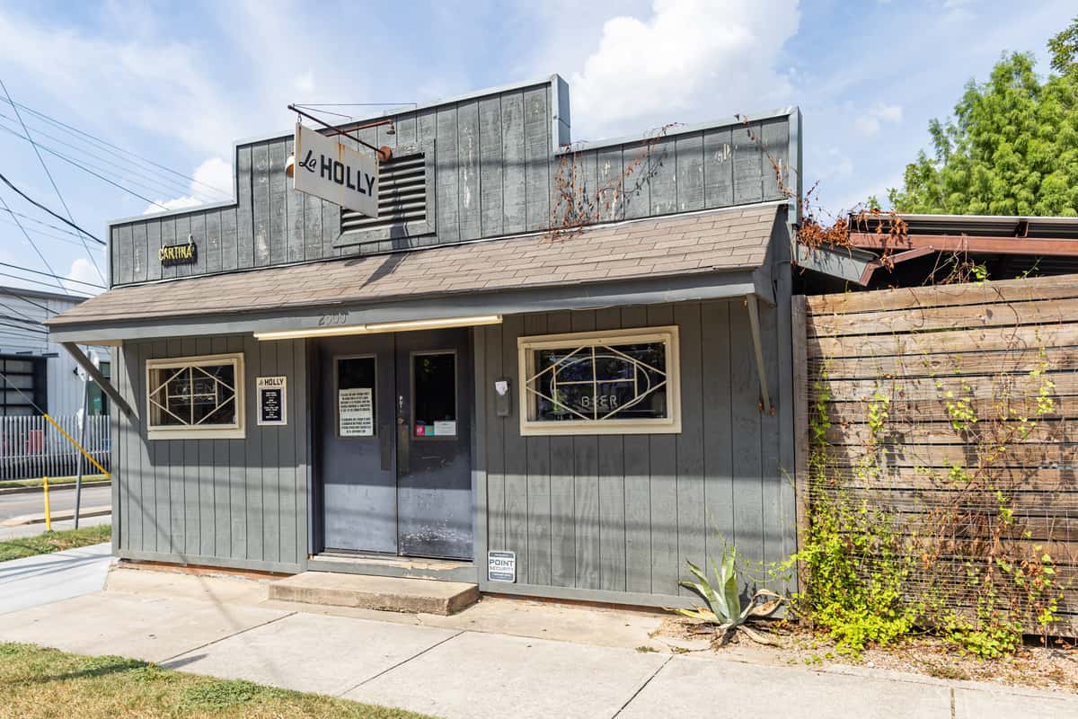 Front view of La Holly cantina in East Austin, featuring a rustic gray wooden facade with vintage-style signage, geometric window grilles, and minimalist curb appeal.