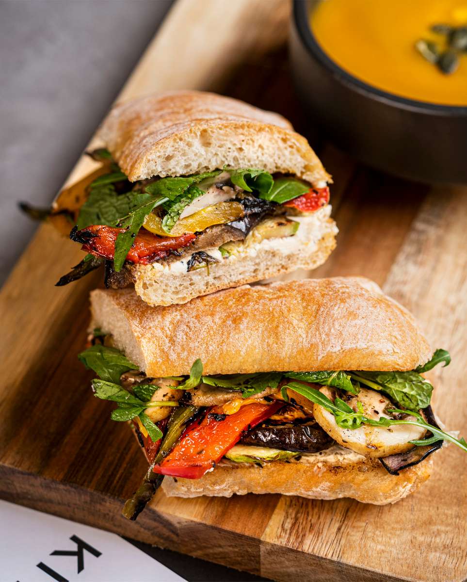 Roasted vegetable sandwich with grilled peppers, mushrooms, zucchini, fresh herbs, and creamy spread on ciabatta bread.