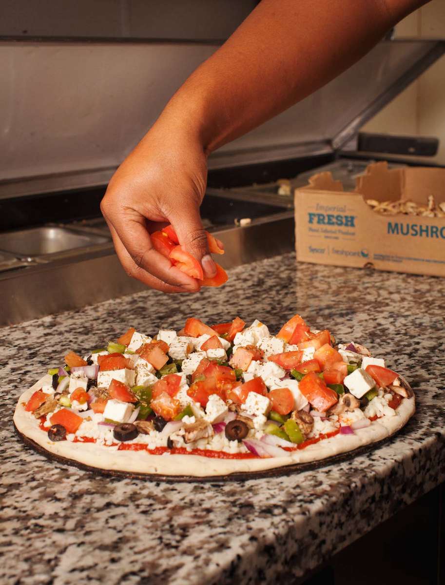 A hand adding toppings to a pizza