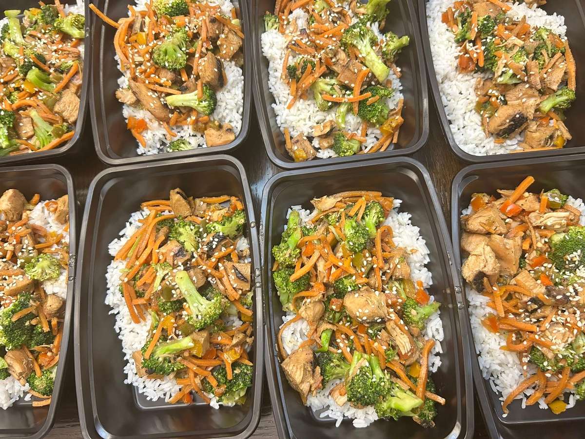 Grilled chicken stir-fry with carrots, broccoli, and sesame seeds served over steamed white rice in meal prep containers.