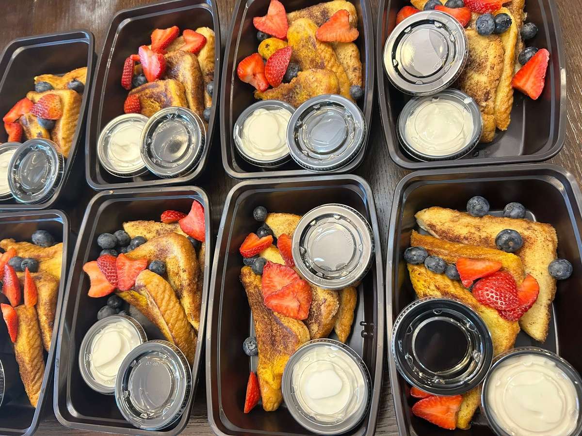 French toast meal prep containers with sliced strawberries, blueberries, and individual syrup and cream sauce portions.