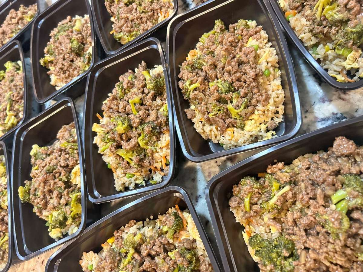 Ground beef and broccoli stir fry over fried rice in black meal prep containers.