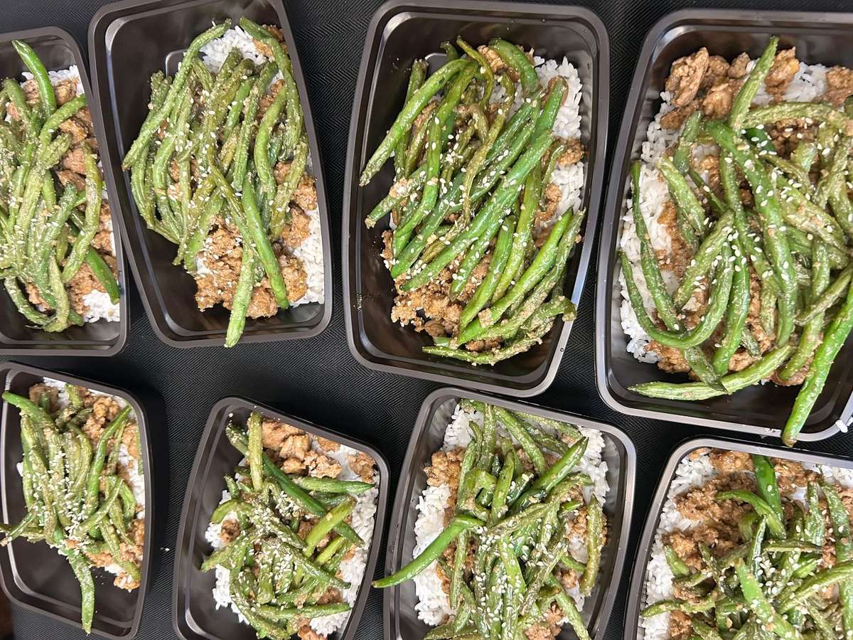 Here's a meal prep layout featuring white rice topped with seasoned ground meat, sautéed green beans, and a sprinkle of sesame seeds.