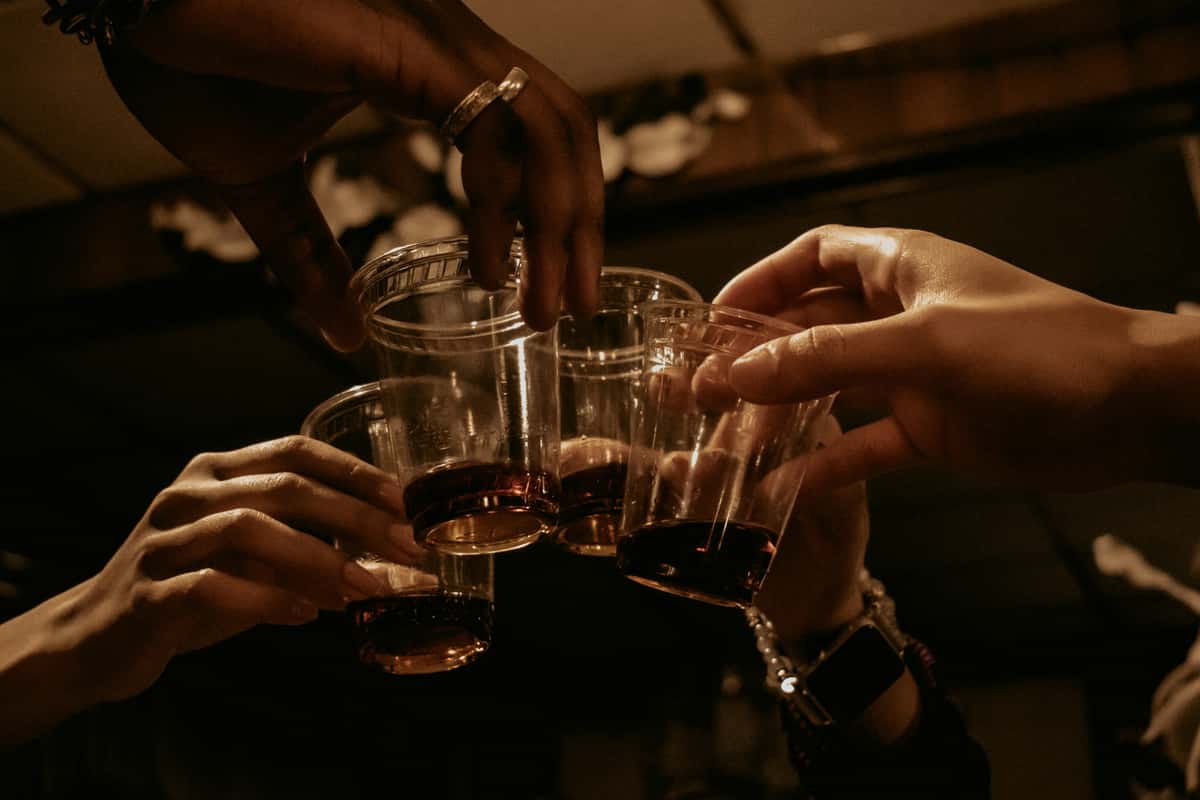 Several hands holding plastic cups filled with dark liquid, clinking together in celebration.