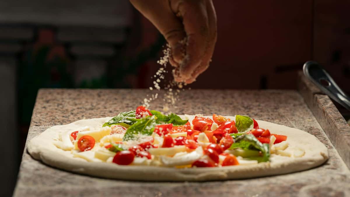 Sprinkling cheese on a pizza about to be baked