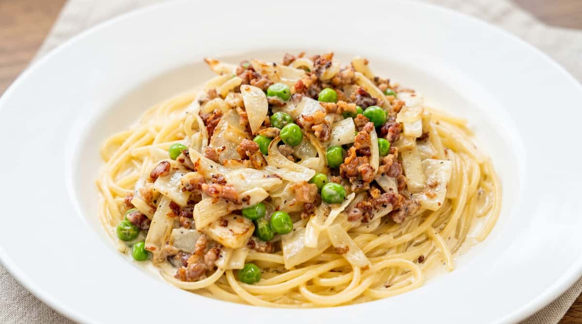 Spaghetti with creamy white sauce, green peas, and diced onions or similar vegetables.