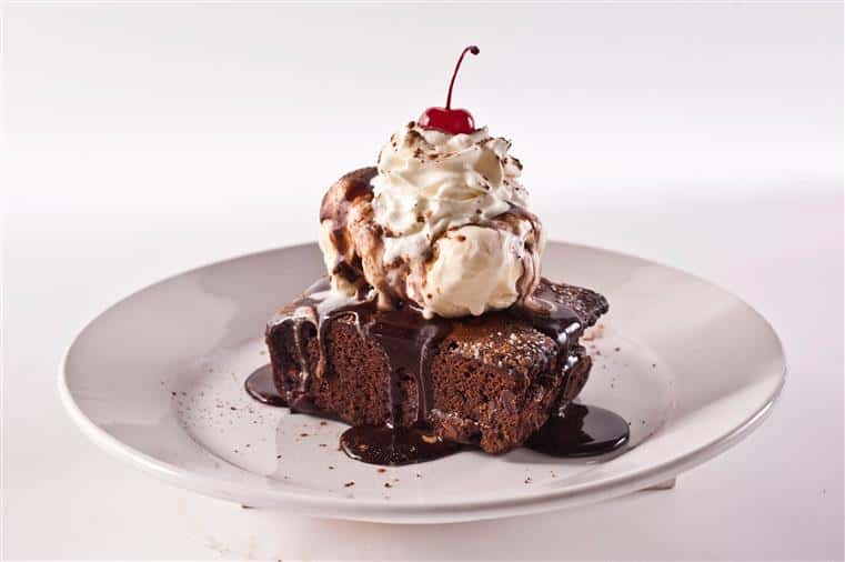 brownie with ice cream and whipped cream on top. a cherry is on top of the whipped cream. brownie is covered in chocolate syrup.