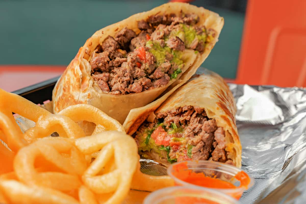 A delicious looking burrito, sliced in half, sits on a tray with fries and two small sauce containers at Señor Burrito Company