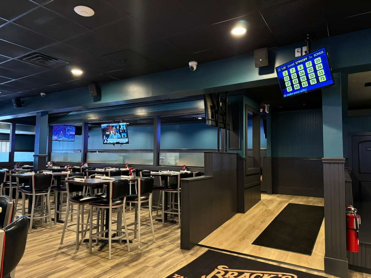 Modern sports bar dining room with high-top tables, multiple TVs showing live sports, and casual seating in a contemporary entertainment venue.