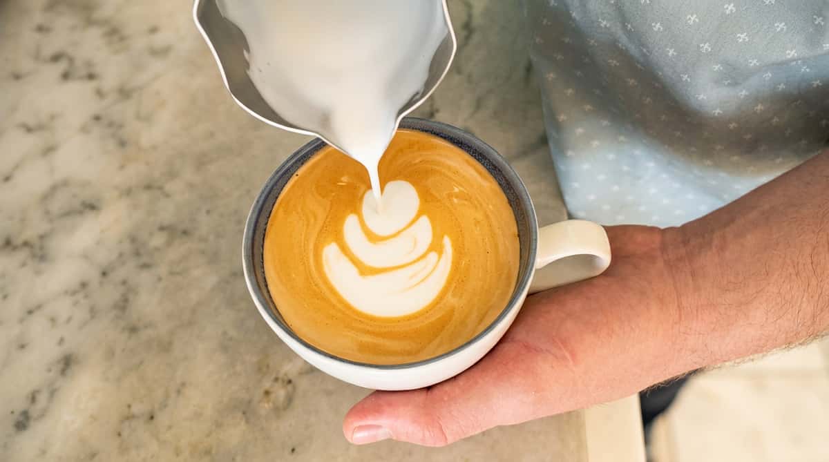 Cafe Remedy | Latte art being poured into a coffee cup, forming a white layered design on a brown surface.