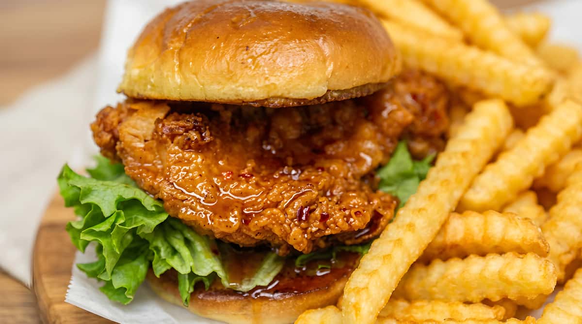 Fried chicken sandwich on a brioche bun with lettuce, served with crinkle-cut fries.