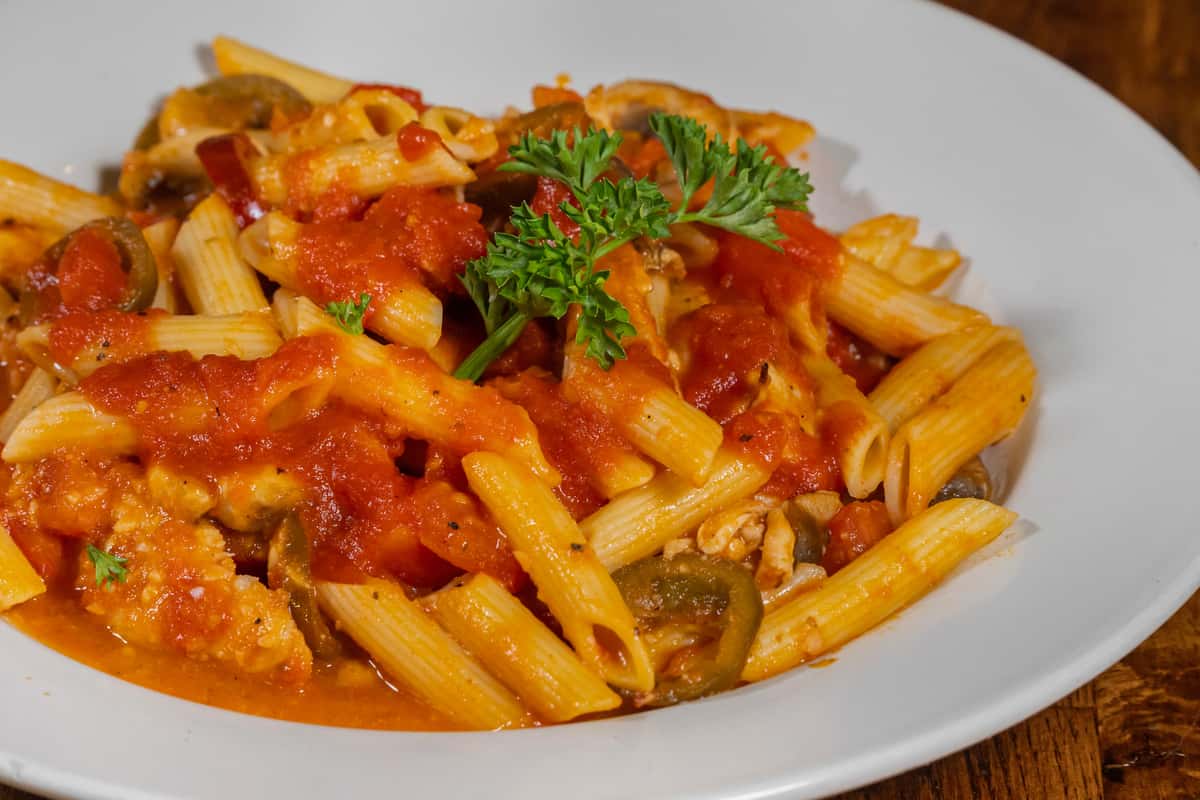 Penne pasta tossed in a zesty marinara sauce with sautéed peppers, onions, and chunks of chicken, garnished with fresh parsley on a white plate.