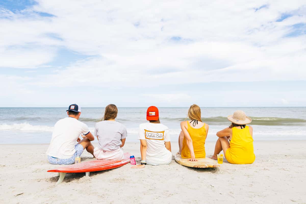 Group of people sitting on the beach, enjoying the ocean view; a relaxed vibe with sun-kissed sand and distant waves.