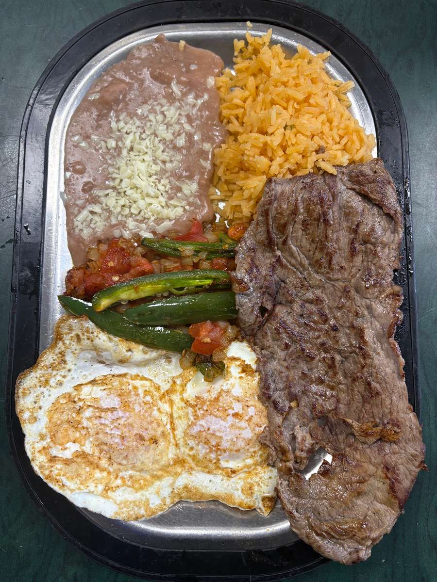 Grilled steak platter with two sunny-side-up eggs, refried beans topped with cheese, Mexican rice, and sautéed jalapeños with salsa.