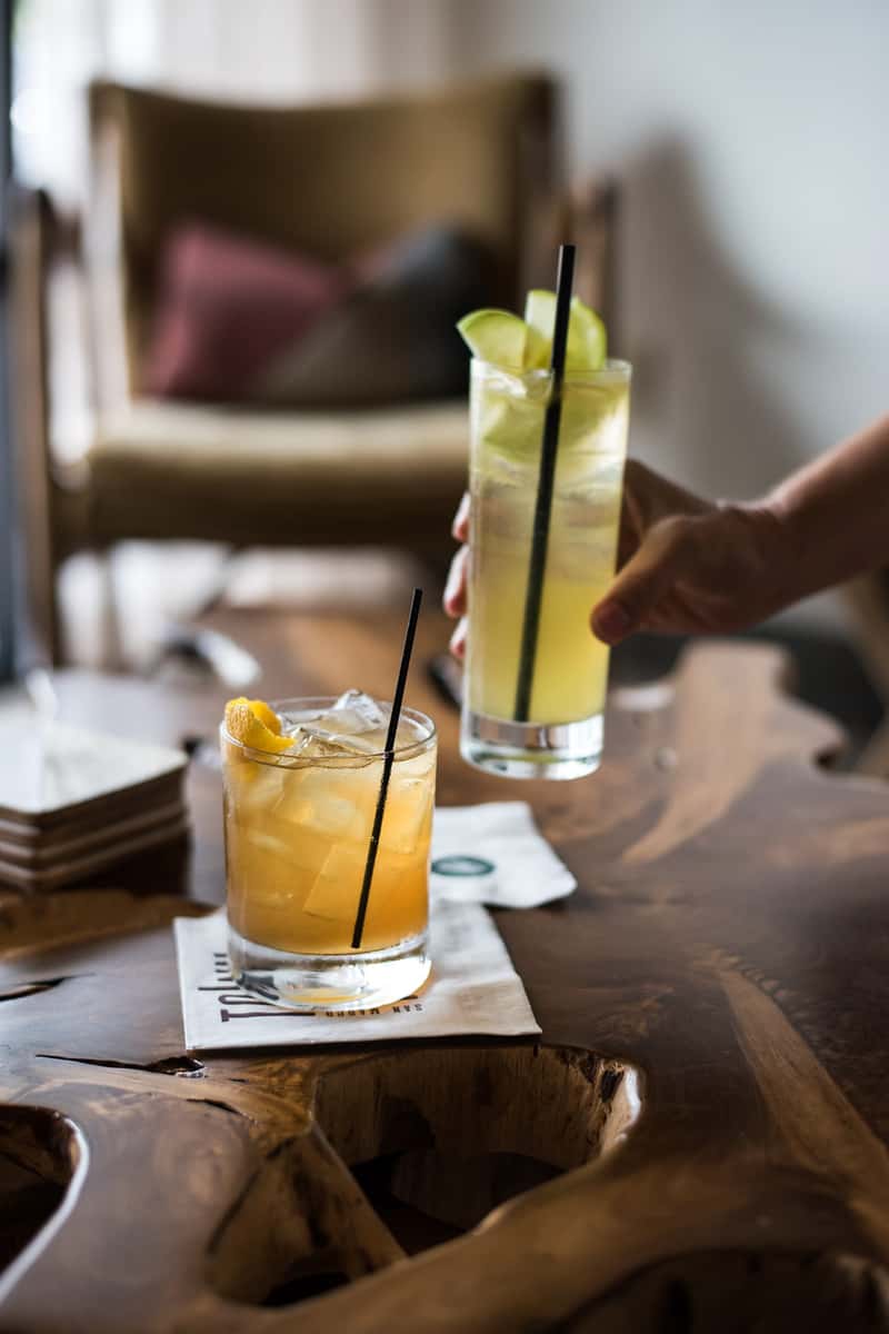Two colorful cocktails in the lounge area of Town Hall restaurant, one on a branded cocktail napkin on a table, one held in a hand.