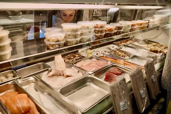 Seafood market case with employee reaching in for haddock, also displaying swordfish, tuna and prepared items