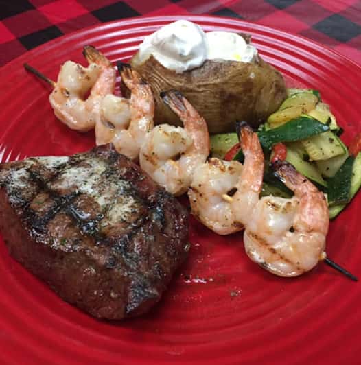 steak, skewer of shrimp, baked potato and vegetables on a plate