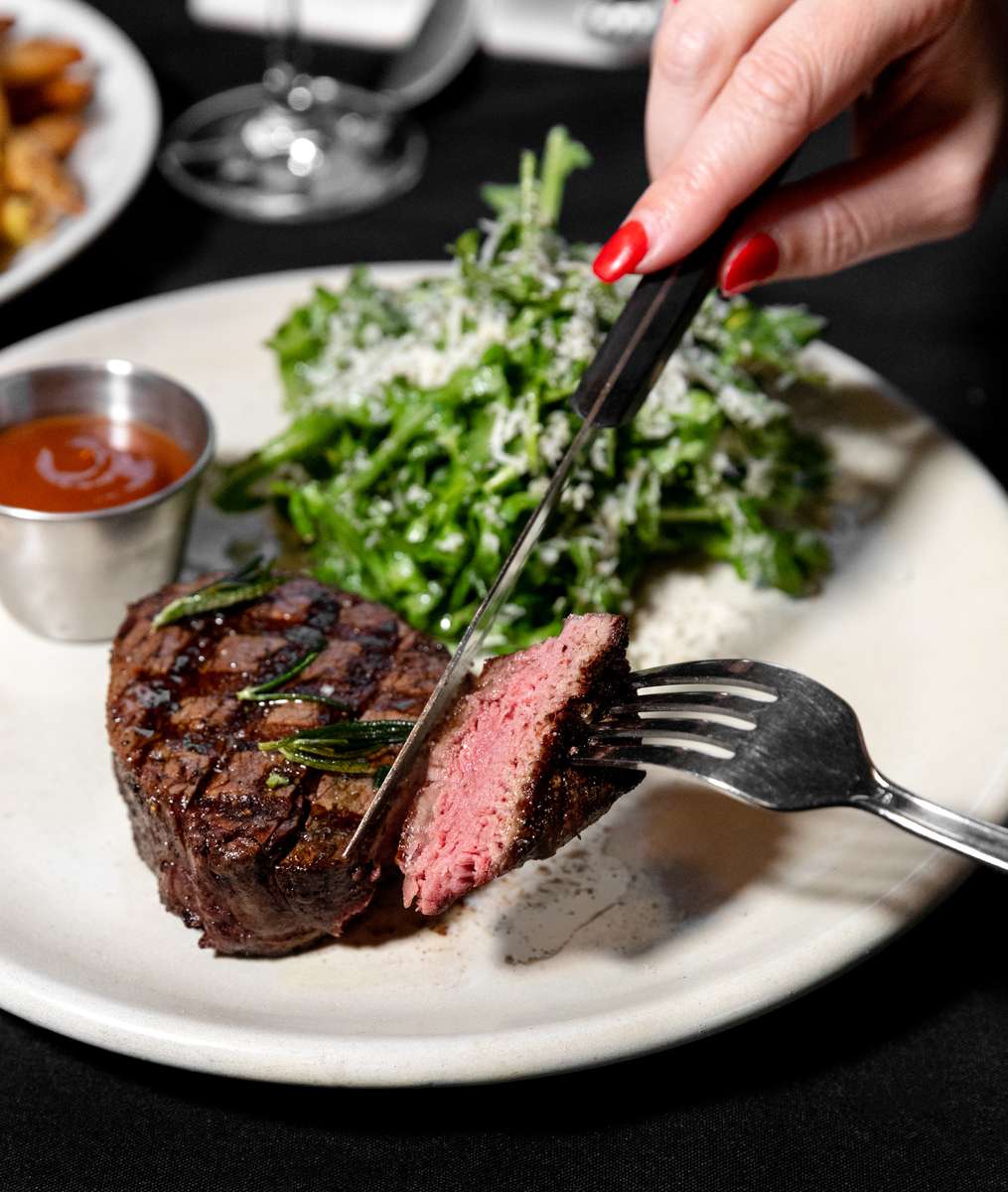 A perfectly cooked steak sliced to reveal a juicy, tender pink center, topped with fresh herbs and served alongside a crisp green salad—an elegant, high-quality dish that highlights rich flavor and expert preparation.
