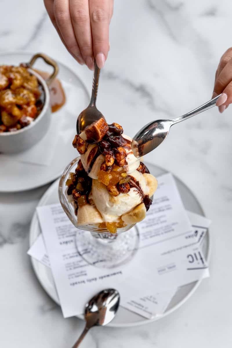 A decadent dessert featuring warm, golden bread pudding drizzled with rich chocolate and caramel sauce, topped with a scoop of creamy vanilla ice cream—an indulgent, sweet finish to any meal.