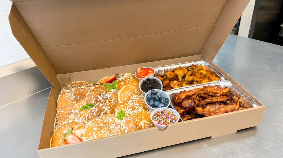 Breakfast box with assorted items including pancakes, fruit, and breakfast sides.