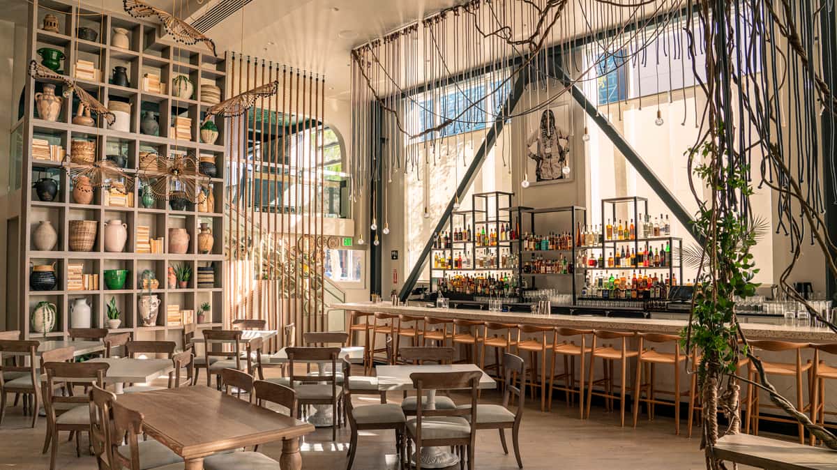 Spacious upscale restaurant interior with modern architecture, communal seating, and tropical-inspired decor
