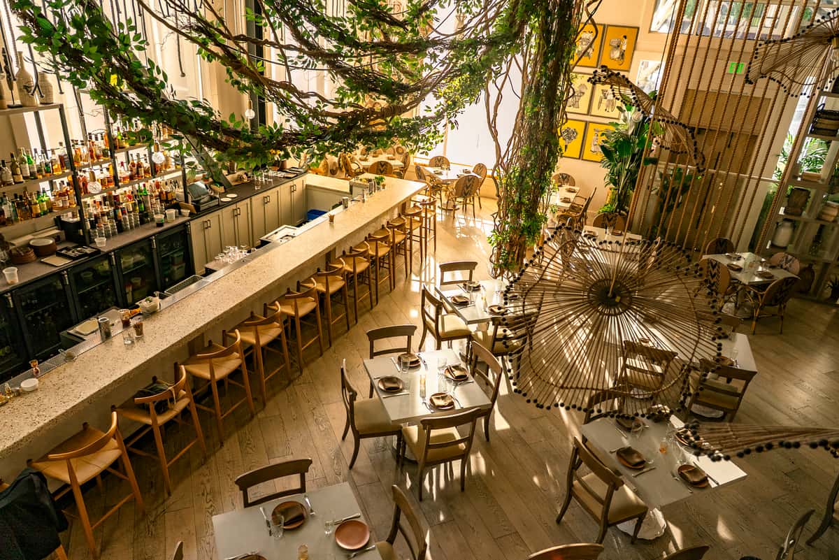 Large tropical-inspired restaurant interior with hanging greenery, communal seating, and elegant modern decor