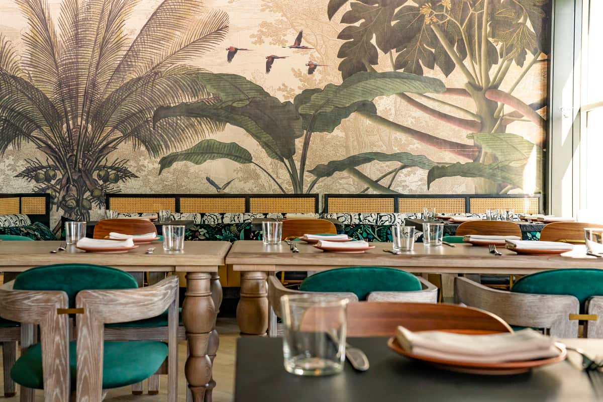 Upscale restaurant dining area with tropical mural artwork, teal seating, and elegant modern interior design