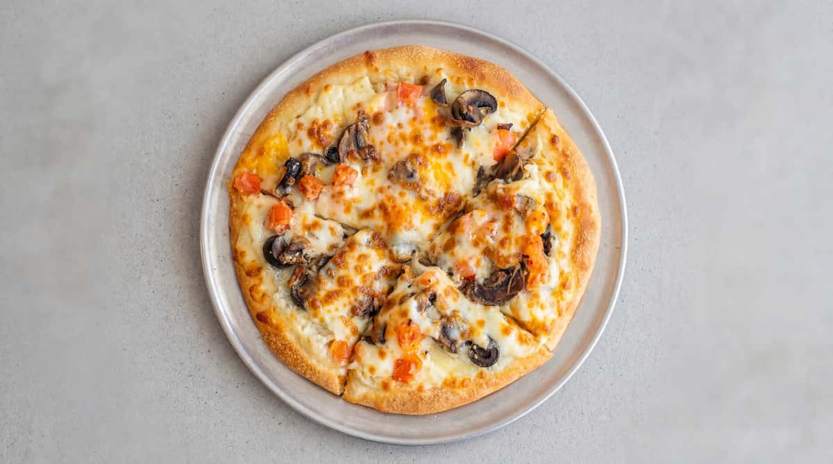 Pizza topped with melted cheese, diced tomatoes, black olives, and mushrooms, on a metal pan.