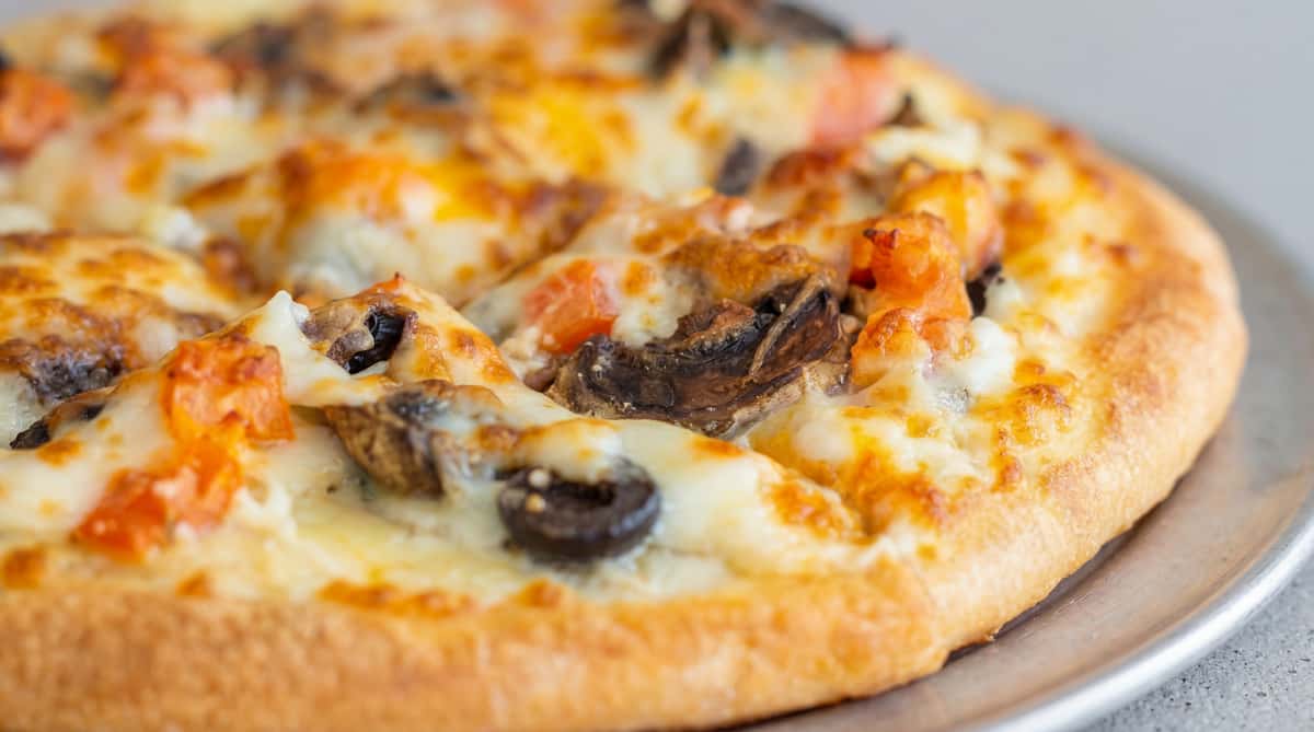 Small round pizza with melted white cheese and a golden-brown topping, on a red background.