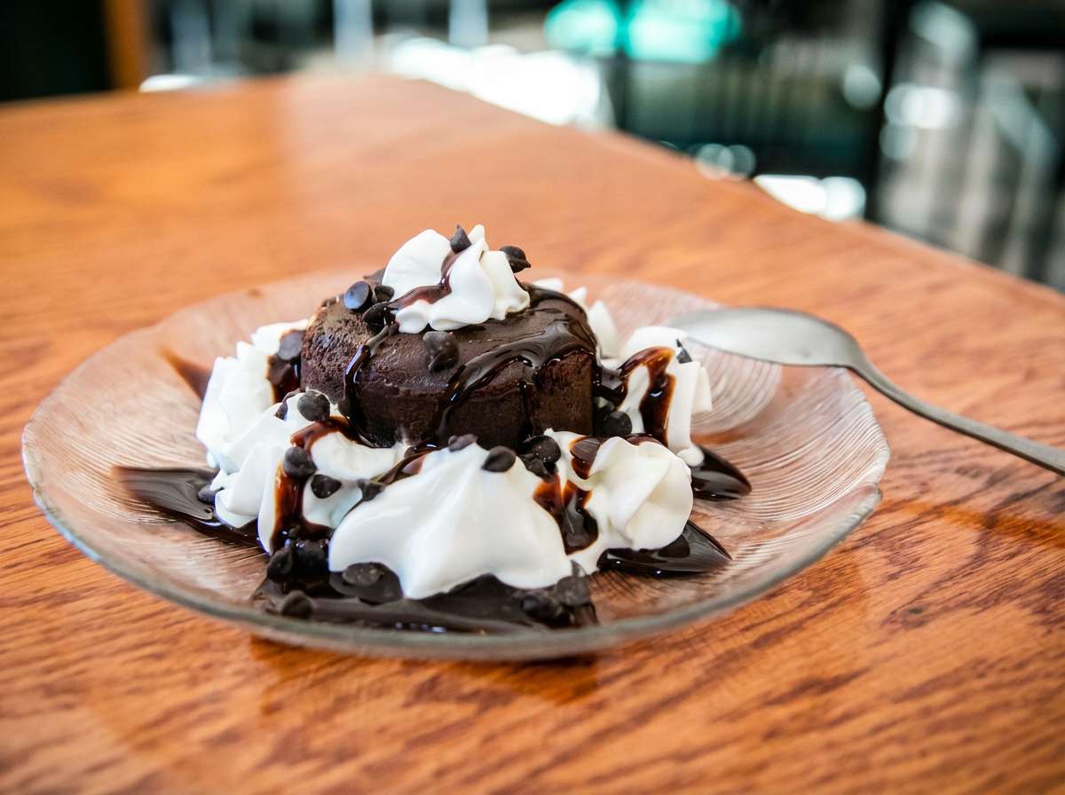 Chocolate brownie topped with whipped cream, chocolate syrup, and mini chocolate chips on a clear plate.