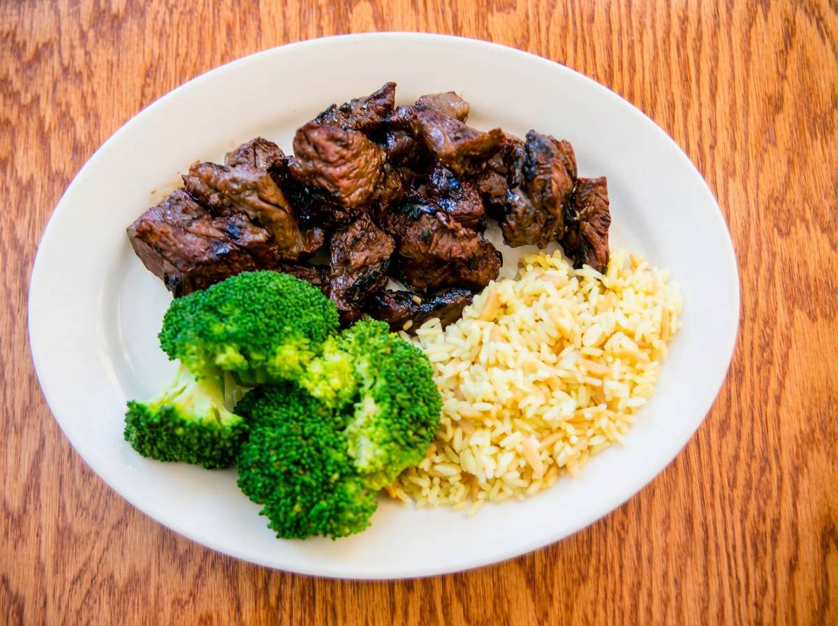 Grilled steak bites with green broccoli and long grain rice on a white plate.