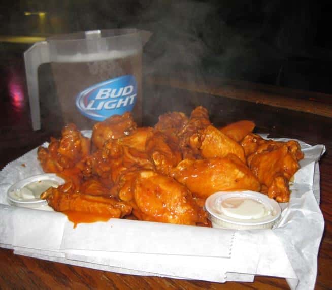 buffalo chicken wings on a platter with a side of blue cheese and a pitcher of bud light 