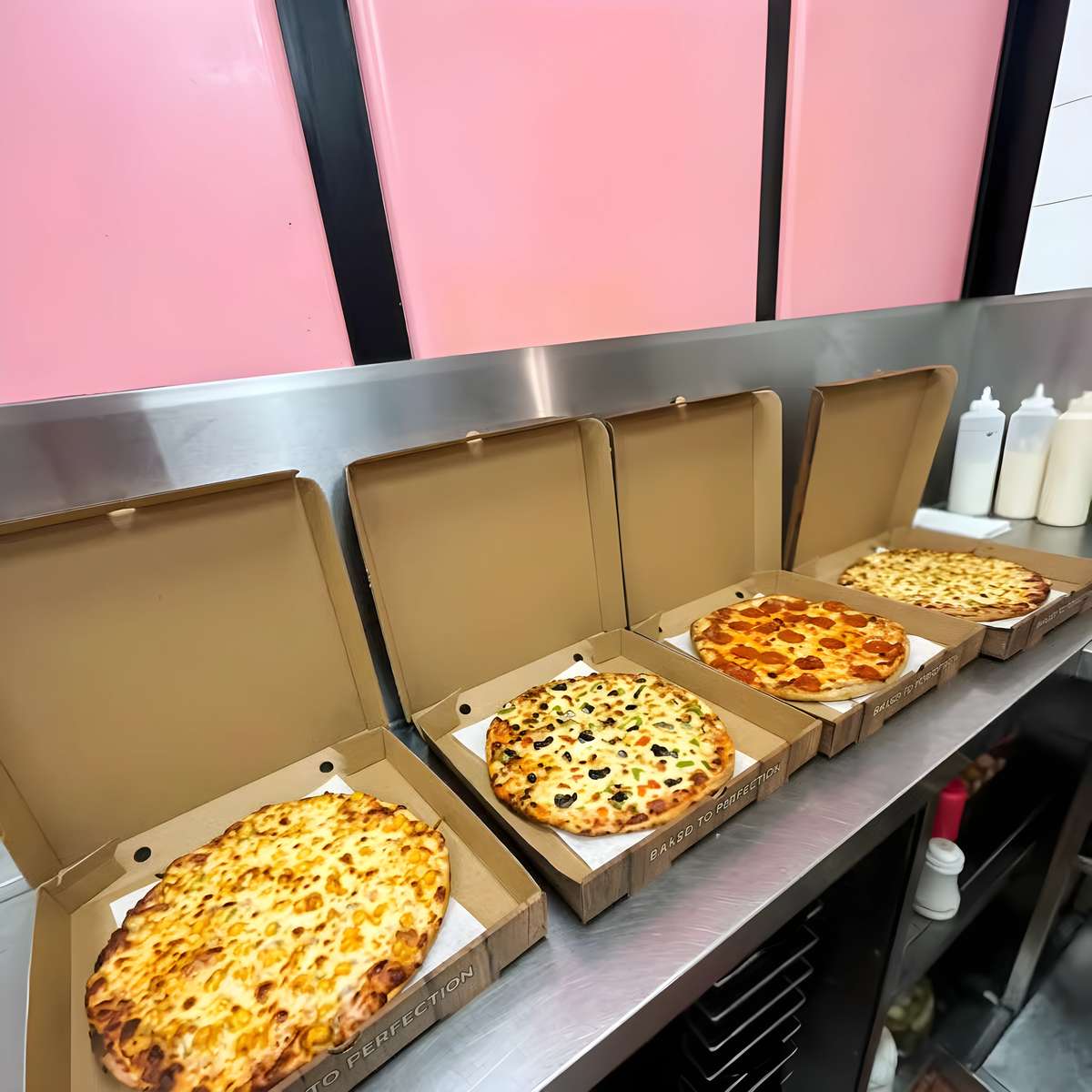 Freshly baked cheese, vegetable, and pepperoni pizzas displayed in takeaway boxes at a pizzeria