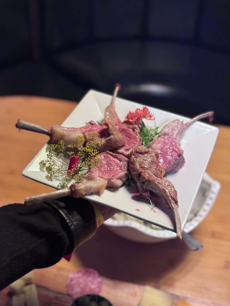Platter of seared lamb chops garnished with fresh herbs and edible flowers, served on a white plate at The Grove Cucina & Wine.
