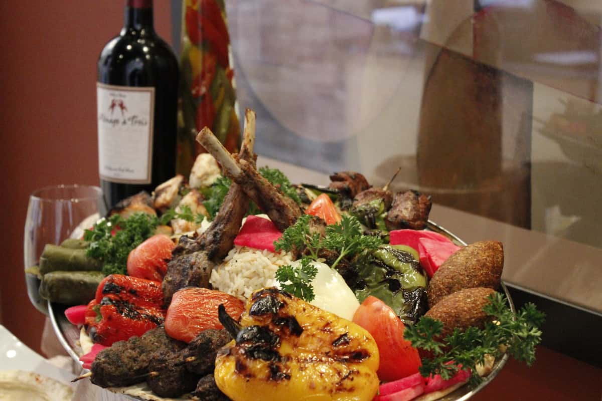 Mediterranean platter featuring grilled meats, fresh vegetables, hummus, and rice.