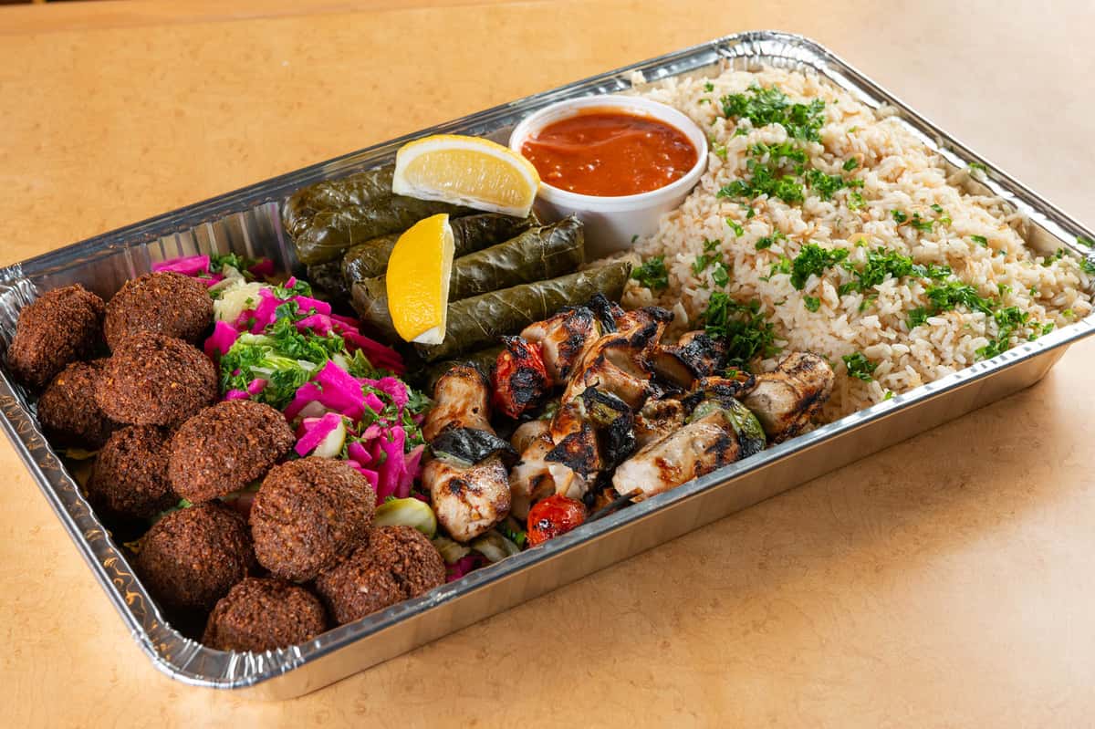 Mediterranean catering trays with grilled meats, falafel, rice, salad, sauces, and pita bread